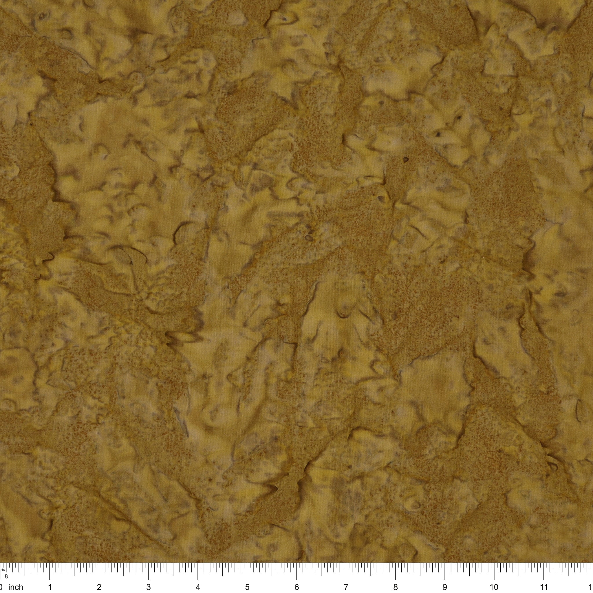 A close-up of a textured material swatch in warm tan and brown tones, with a ruler scale visible along the bottom edge.