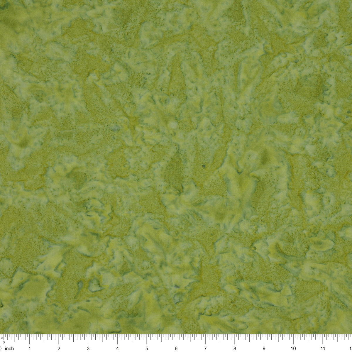 A close-up of a textured fabric in mottled olive green and yellow-green tones, with a ruler along the bottom edge showing scale.