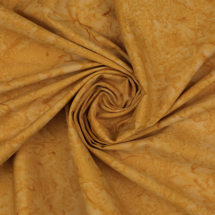 A close-up of draped fabric with a marbled pattern in warm golden yellow and tan tones, arranged in a spiral fold.