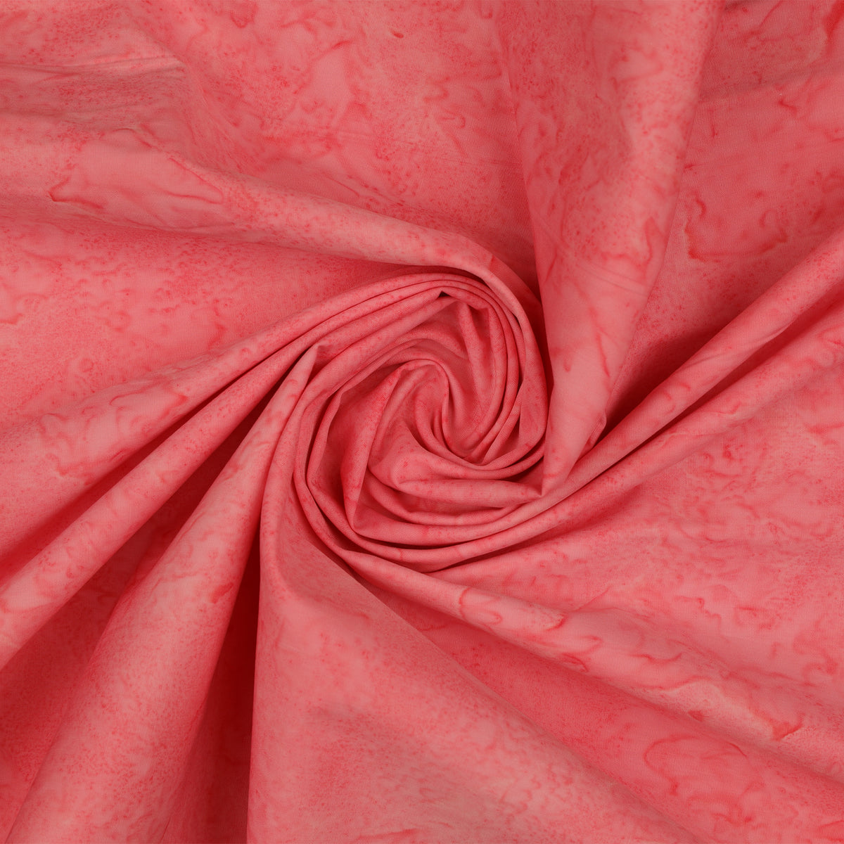 A close-up of coral pink fabric with a subtle marbled or mottled pattern, arranged in a spiral drape to show texture and color variation.