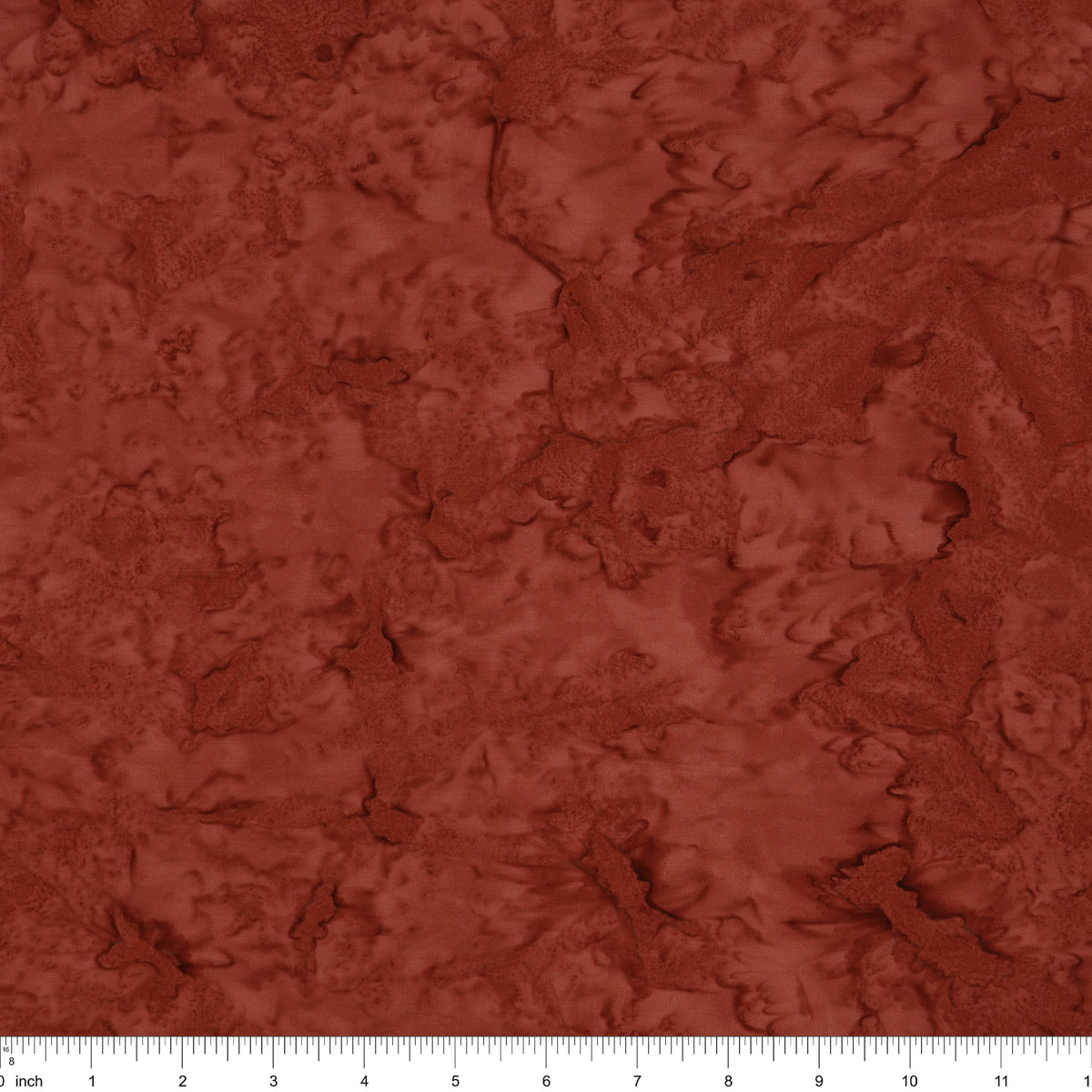A close-up of a textured fabric or material swatch in a warm rust red color, with a ruler scale visible along the bottom edge.