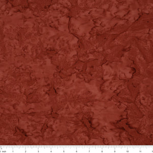 A close-up of a textured fabric or material swatch in a warm rust red color, with a ruler scale visible along the bottom edge.