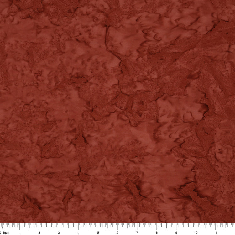 A close-up of a textured fabric or material swatch in a warm rust red color, with a ruler scale visible along the bottom edge.