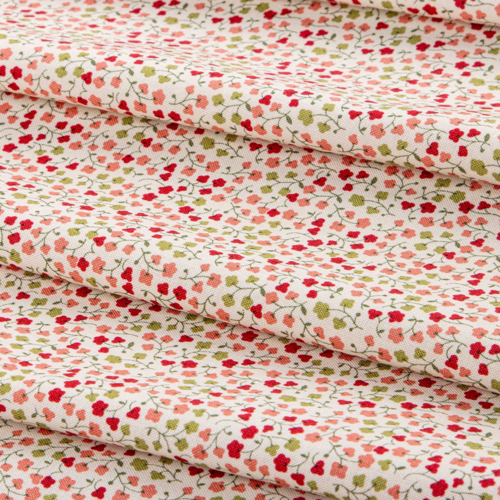 A close-up of folded fabric with a dense small floral print on a warm off-white background. The pattern features red, pink, and light green flowers with thin green stems and leaves.