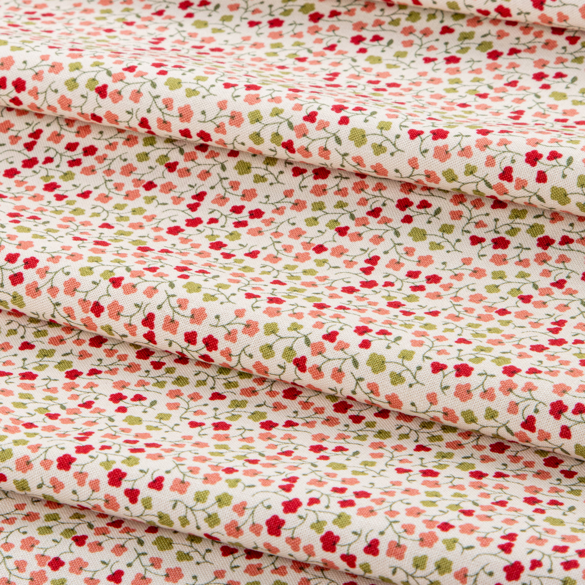 A close-up of folded fabric with a dense small floral print on a warm off-white background. The pattern features red, pink, and light green flowers with thin green stems and leaves.