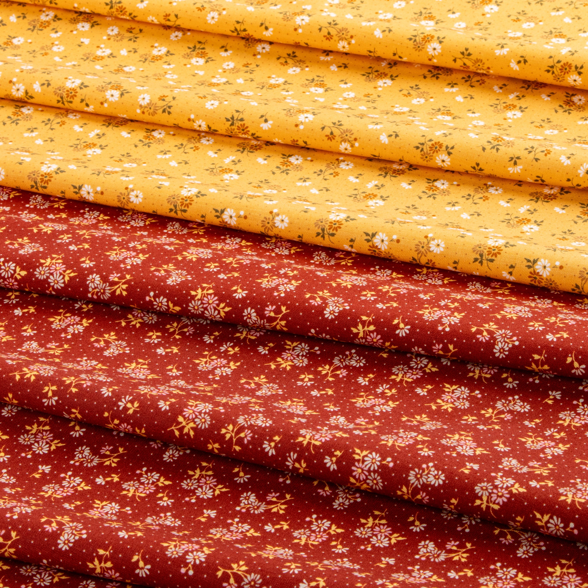 Stacked fabric pieces with a small floral print, showing two main colors: a bright yellow top layer and a rust red bottom layer, both decorated with tiny white flowers and green stems.