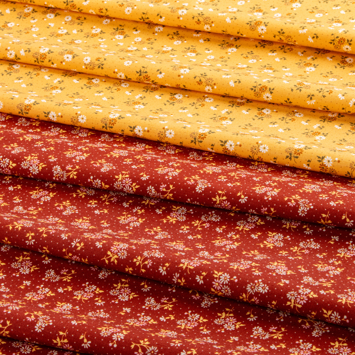 Stacked fabric pieces with a small floral print, showing two main colors: a bright yellow top layer and a rust red bottom layer, both decorated with tiny white flowers and green stems.