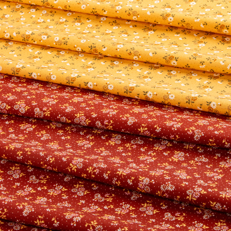 Stacked fabric pieces with a small floral print, showing two main colors: a bright yellow top layer and a rust red bottom layer, both decorated with tiny white flowers and green stems.