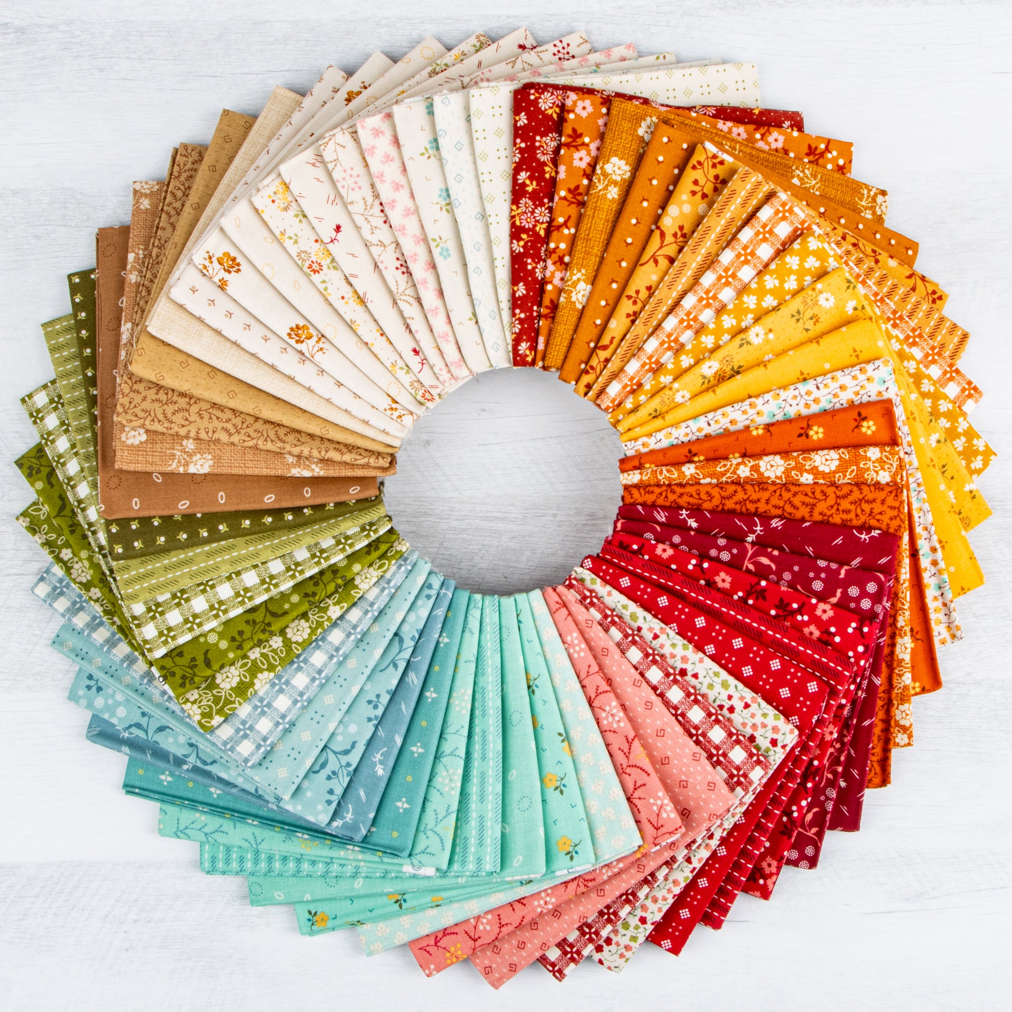 A circular arrangement of folded fabric swatches in many colors and patterns, fanned out on a light gray surface. The fabrics include beige, brown, green, aqua, pink, red, orange, and yellow tones with floral, dot, and paisley prints.