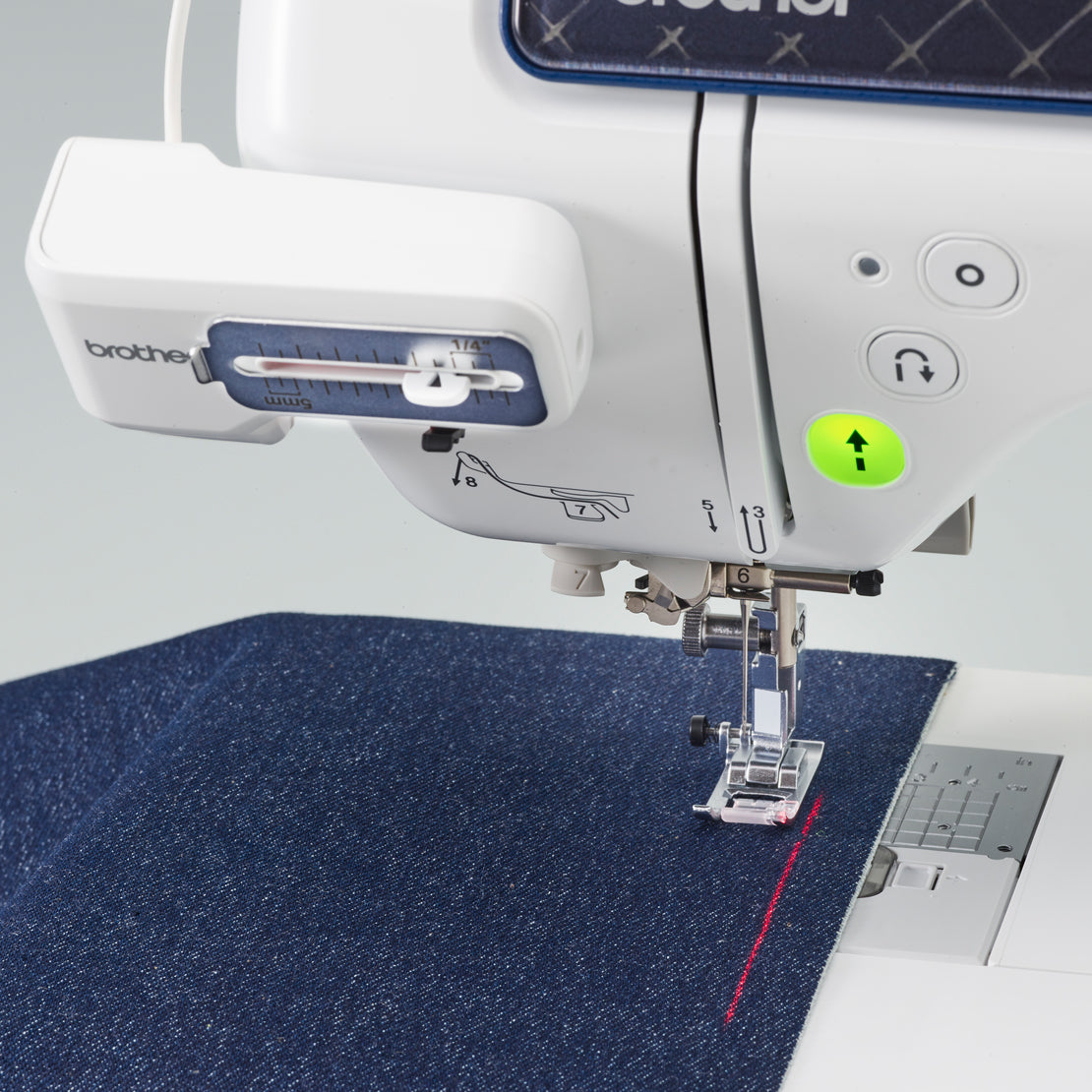 A close-up of a Brother sewing machine stitching a dark blue textured fabric, with the Brother logo visible on the machine arm and a laser guide.