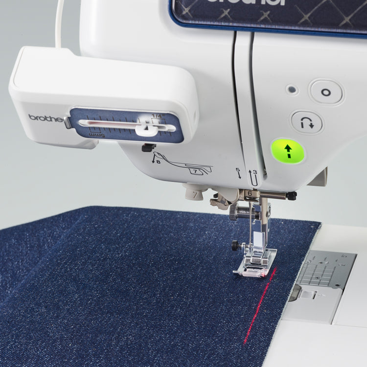 A close-up of a Brother sewing machine stitching a dark blue textured fabric, with the Brother logo visible on the machine arm and a laser guide.