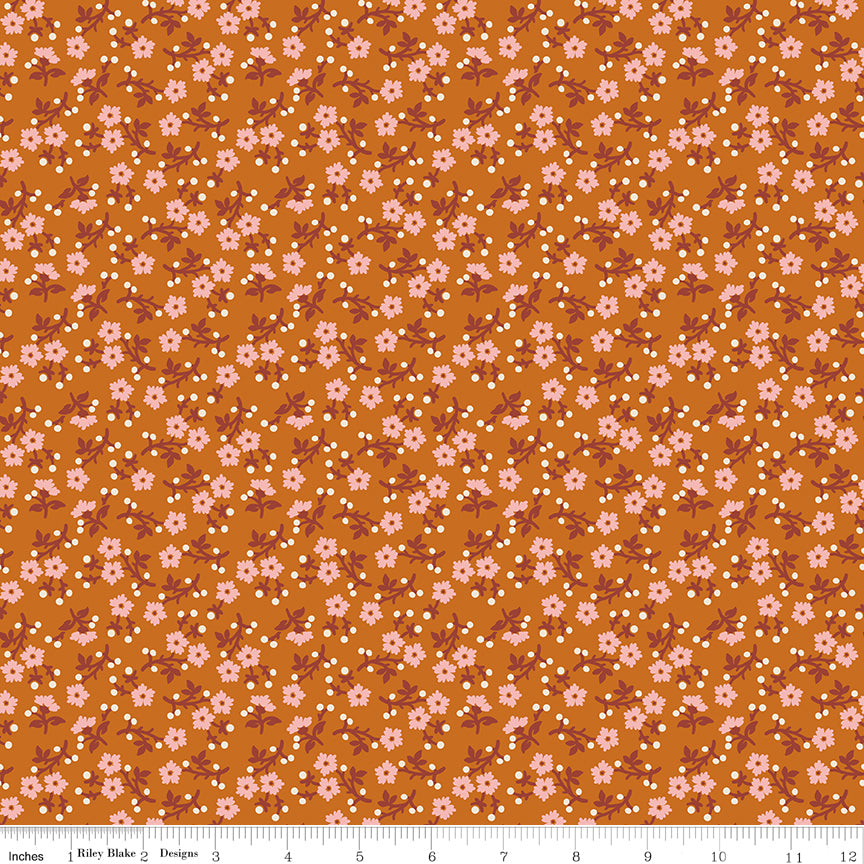A repeating floral pattern on a warm orange-brown background, featuring small pink flowers, white dots, and muted reddish-brown stems. Ruler along the bottom for scale. 