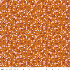 A repeating floral pattern on a warm orange-brown background, featuring small pink flowers, white dots, and muted reddish-brown stems. Ruler along the bottom for scale. 