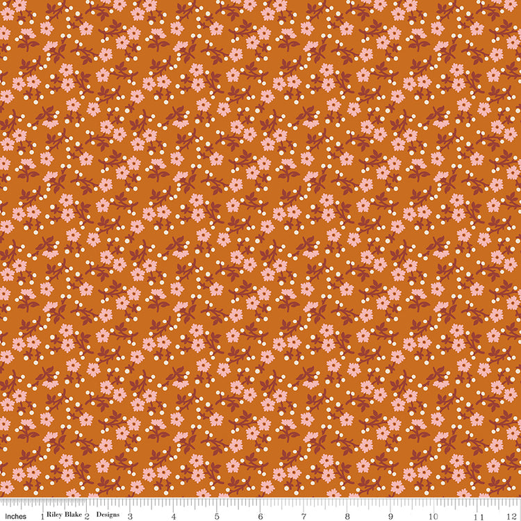 A repeating floral pattern on a warm orange-brown background, featuring small pink flowers, white dots, and muted reddish-brown stems. Ruler along the bottom for scale. 