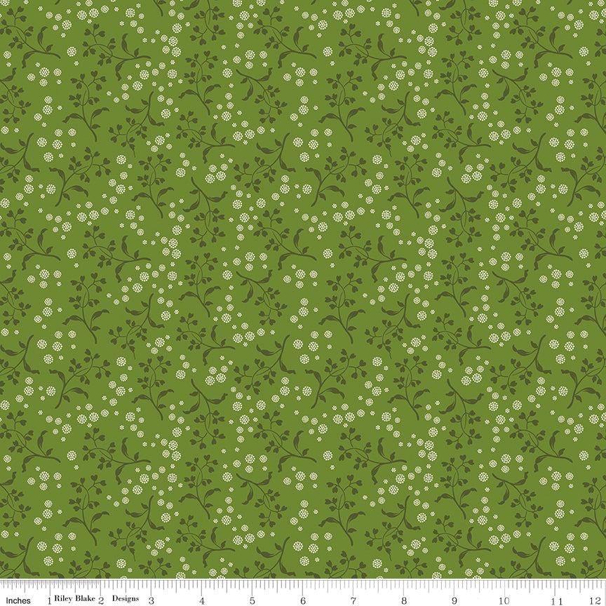 A repeating floral pattern featuring small white flowers and dark green leaves on a medium olive green background. Ruler along the bottom for scale. 
