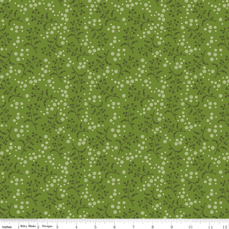 A repeating floral pattern featuring small white flowers and dark green leaves on a medium olive green background. Ruler along the bottom for scale. 