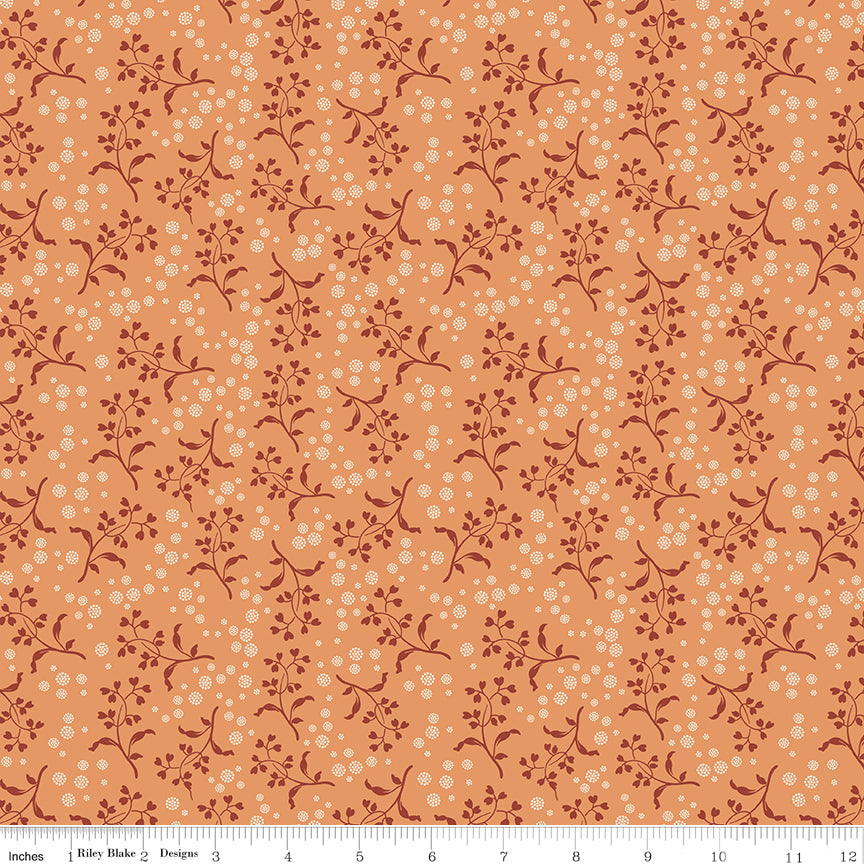 A seamless repeating pattern featuring delicate dark reddish-brown floral vines and small cream-colored dots on a warm peach-orange background. Ruler along the bottom for scale. 