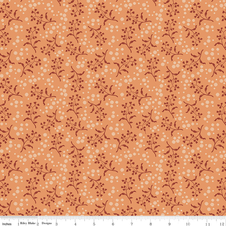 A seamless repeating pattern featuring delicate dark reddish-brown floral vines and small cream-colored dots on a warm peach-orange background. Ruler along the bottom for scale. 