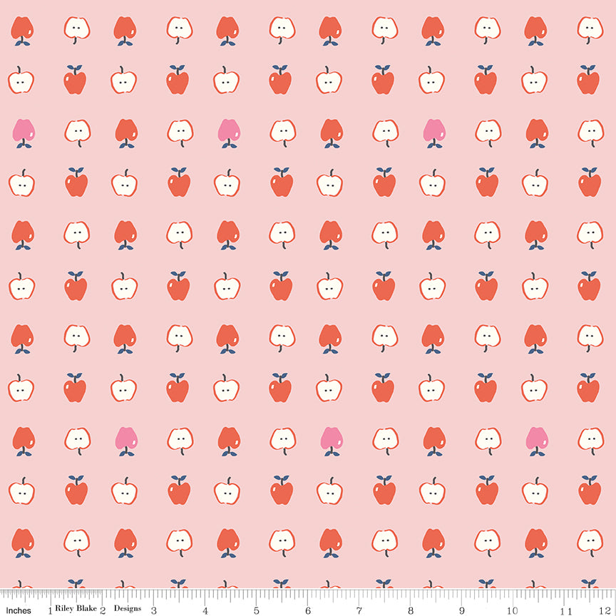 Cotton Nook Apples Pink fabric with red, pink and sliced apples arranged on a soft pink background with ruler for scale.