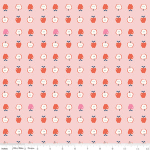 Cotton Nook Apples Pink fabric with red, pink and sliced apples arranged on a soft pink background with ruler for scale.
