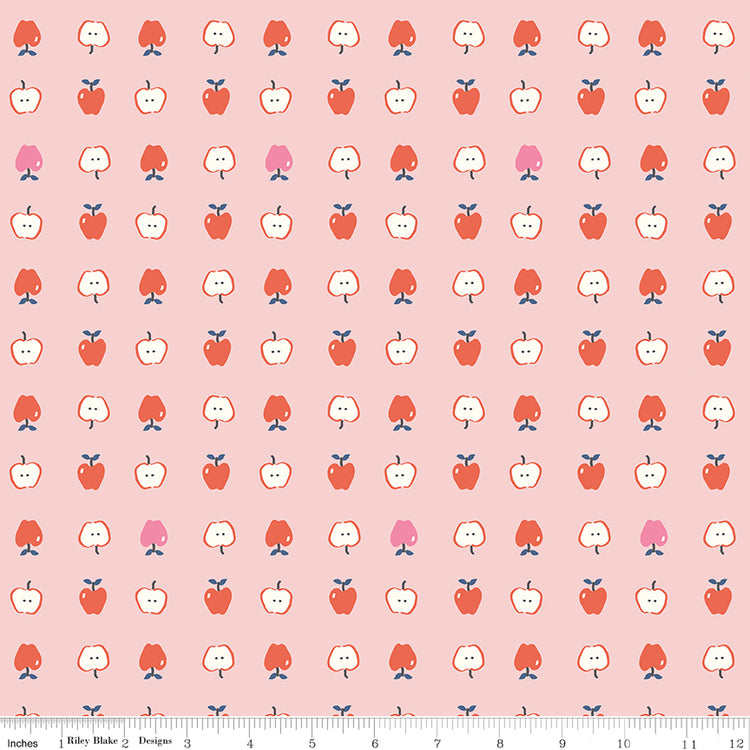 Cotton Nook Apples Pink fabric with red, pink and sliced apples arranged on a soft pink background with ruler for scale.