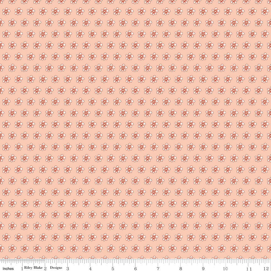 Blush pink fabric with evenly spaced small cream and coral flowers with a ruler for scale