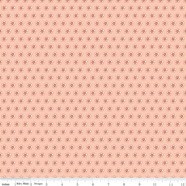 Blush pink fabric with evenly spaced small cream and coral flowers with a ruler for scale