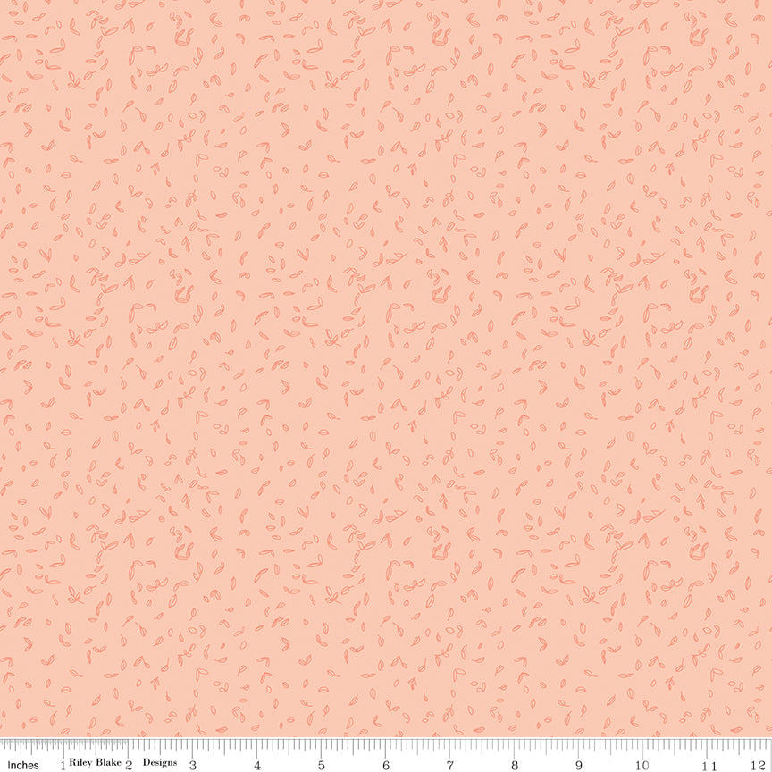 Blush pink fabric with scattered tiny coral leaf motifs and a ruler for scale along the bottom. 