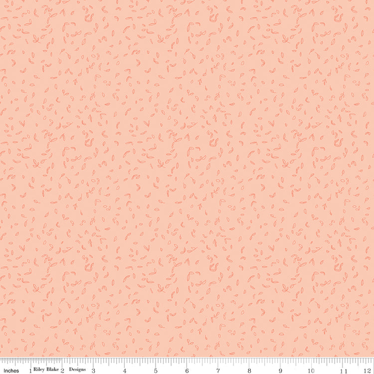 Blush pink fabric with scattered tiny coral leaf motifs and a ruler for scale along the bottom. 