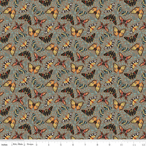 A repeating fabric pattern featuring colorful butterflies in orange, yellow, black, and blue on a muted gray-green background, with a ruler along the bottom edge showing scale.