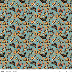 A repeating fabric pattern featuring orange, black, and white butterflies on a muted teal-blue background with small abstract orange scribbles. A ruler along the bottom edge shows scale.