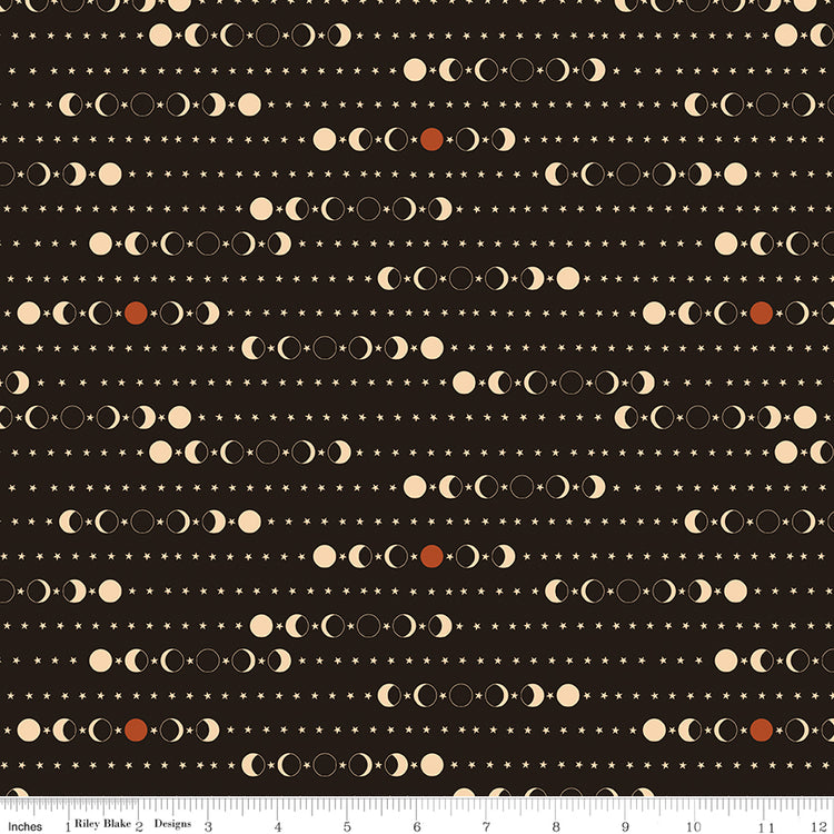 A repeating celestial pattern of moon phases, stars, and dots on a dark brown background, with a fabric ruler for scale.