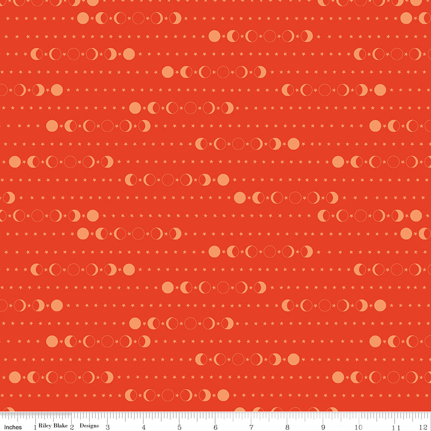 A close-up of a fabric pattern featuring repeating rows of moon phases and small stars on a warm orange-red background, with a ruler along the bottom edge showing scale.