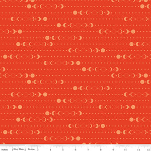 A close-up of a fabric pattern featuring repeating rows of moon phases and small stars on a warm orange-red background, with a ruler along the bottom edge showing scale.