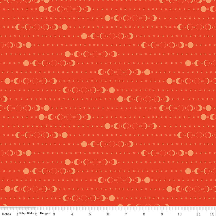 A close-up of a fabric pattern featuring repeating rows of moon phases and small stars on a warm orange-red background, with a ruler along the bottom edge showing scale.