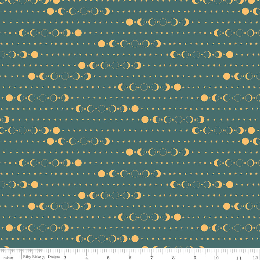 A repeating celestial pattern of sun and moon phases and small stars on a muted teal fabric background, shown with a ruler at the bottom indicating scale.