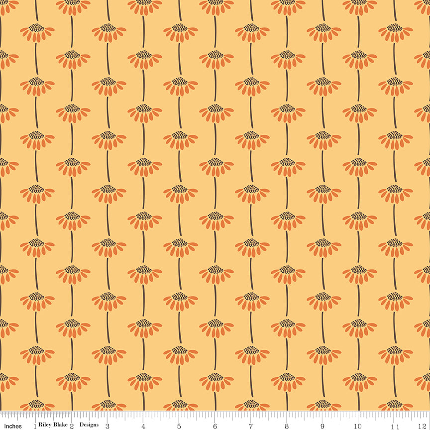 A repeating floral pattern on fabric with orange flower heads, dark brown centers and stems, and a warm peach background. A ruler along the bottom edge shows the scale of the print.