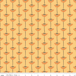 A repeating floral pattern on fabric with orange flower heads, dark brown centers and stems, and a warm peach background. A ruler along the bottom edge shows the scale of the print.