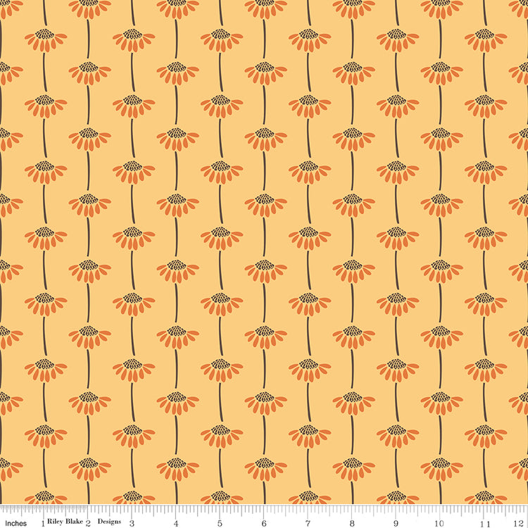 A repeating floral pattern on fabric with orange flower heads, dark brown centers and stems, and a warm peach background. A ruler along the bottom edge shows the scale of the print.