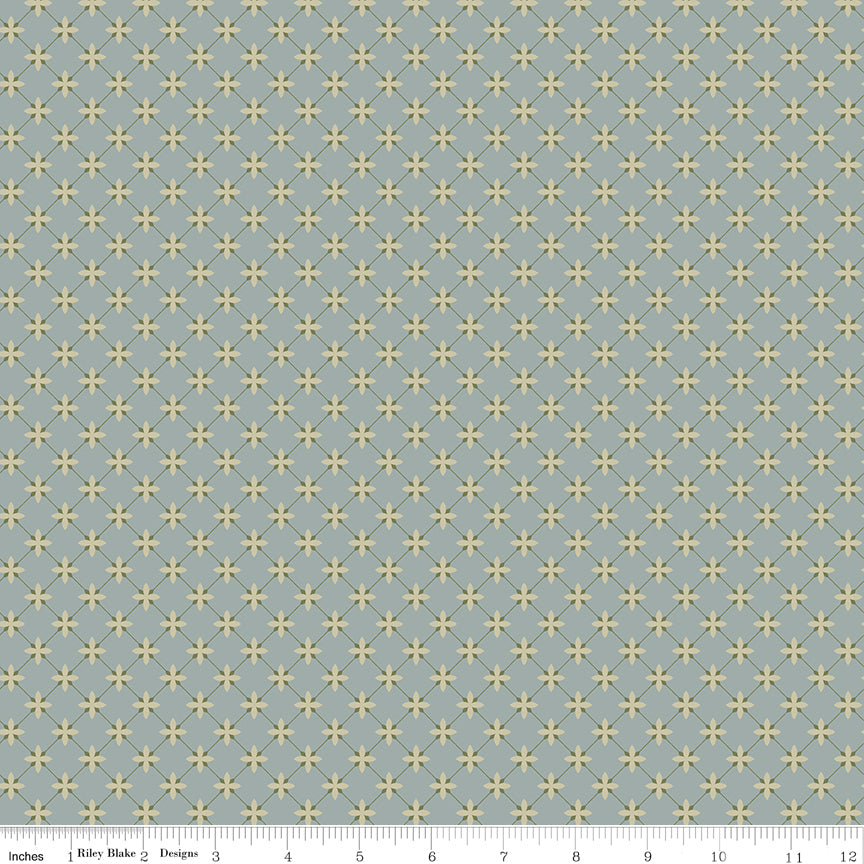 Stella Dove fabric with pale yellow four-petal flowers and an olive diamond lattice on blue-gray with ruler for scale.
