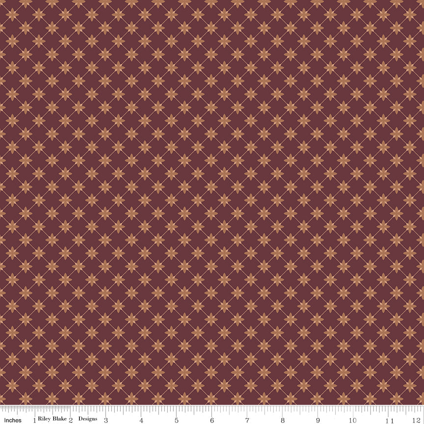 Stella Mahogany fabric with clay-colored four-petal flowers in a diamond lattice on burgundy brown with ruler for scale.