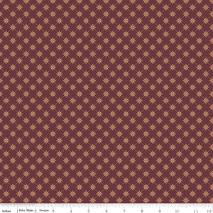 Stella Mahogany fabric with clay-colored four-petal flowers in a diamond lattice on burgundy brown with ruler for scale.