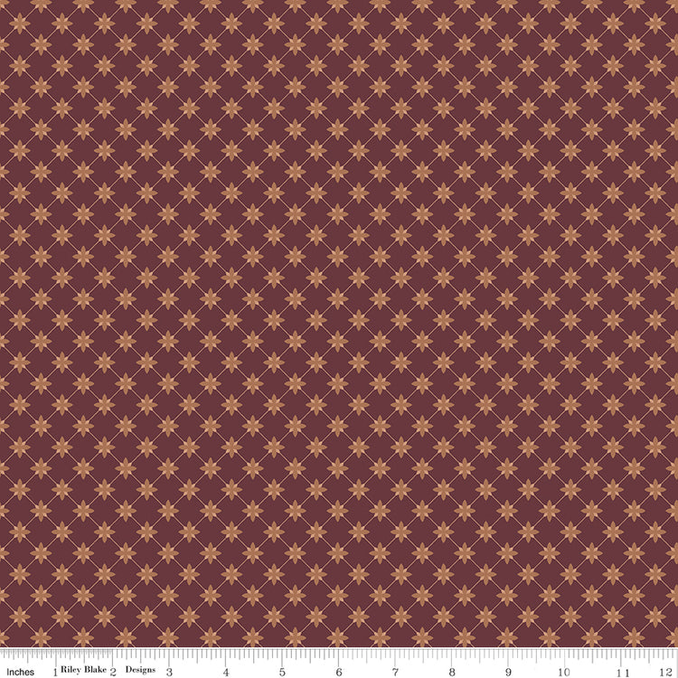 Stella Mahogany fabric with clay-colored four-petal flowers in a diamond lattice on burgundy brown with ruler for scale.
