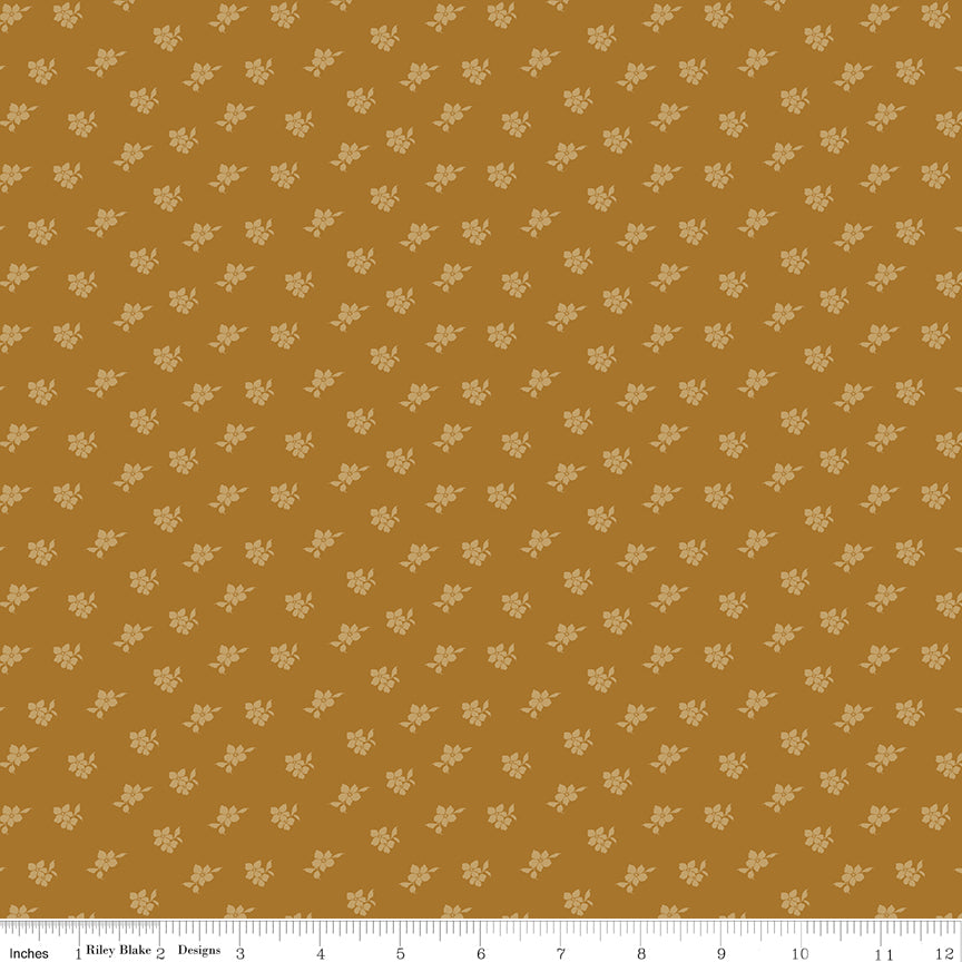 Magnolia Suede fabric with tiny pale golden flowers and leaves scattered on a caramel-brown background with ruler for scale.