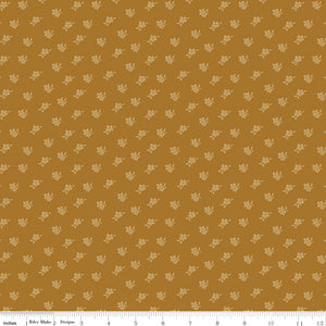 Magnolia Suede fabric with tiny pale golden flowers and leaves scattered on a caramel-brown background with ruler for scale.