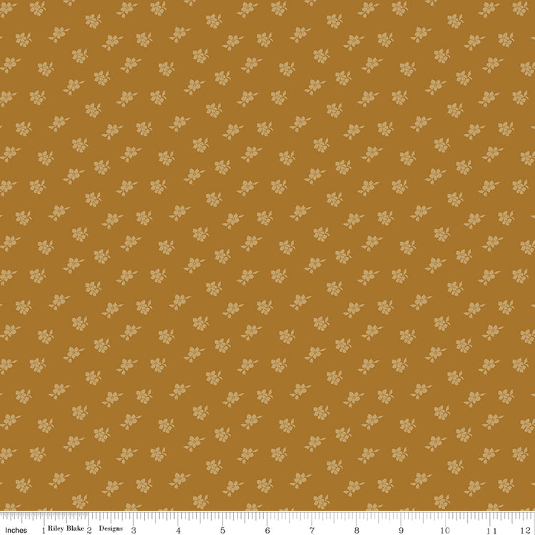 Magnolia Suede fabric with tiny pale golden flowers and leaves scattered on a caramel-brown background with ruler for scale.