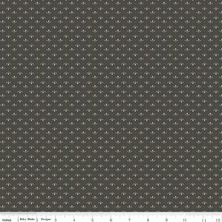Lottie Gray fabric with tiny cream leaf sprigs and dots in alternating rows on a dark warm gray background with ruler for scale.