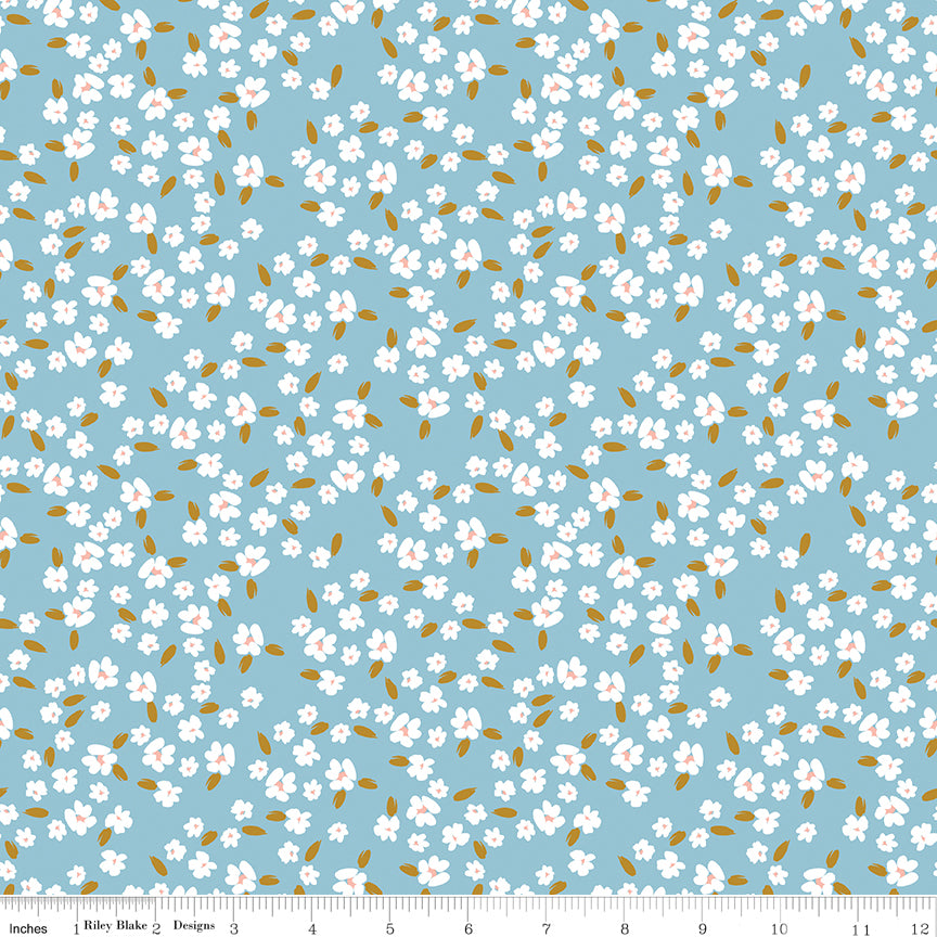 Blossoms Dream fabric with white flowers, pale pink centers, and golden leaves on a light blue background with ruler for scale.