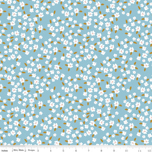 Blossoms Dream fabric with white flowers, pale pink centers, and golden leaves on a light blue background with ruler for scale.