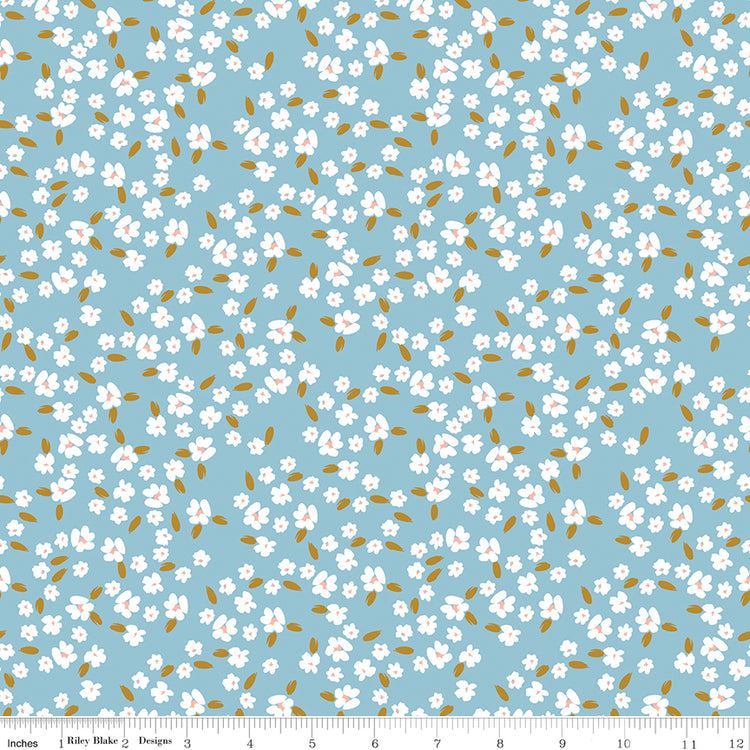Blossoms Dream fabric with white flowers, pale pink centers, and golden leaves on a light blue background with ruler for scale.